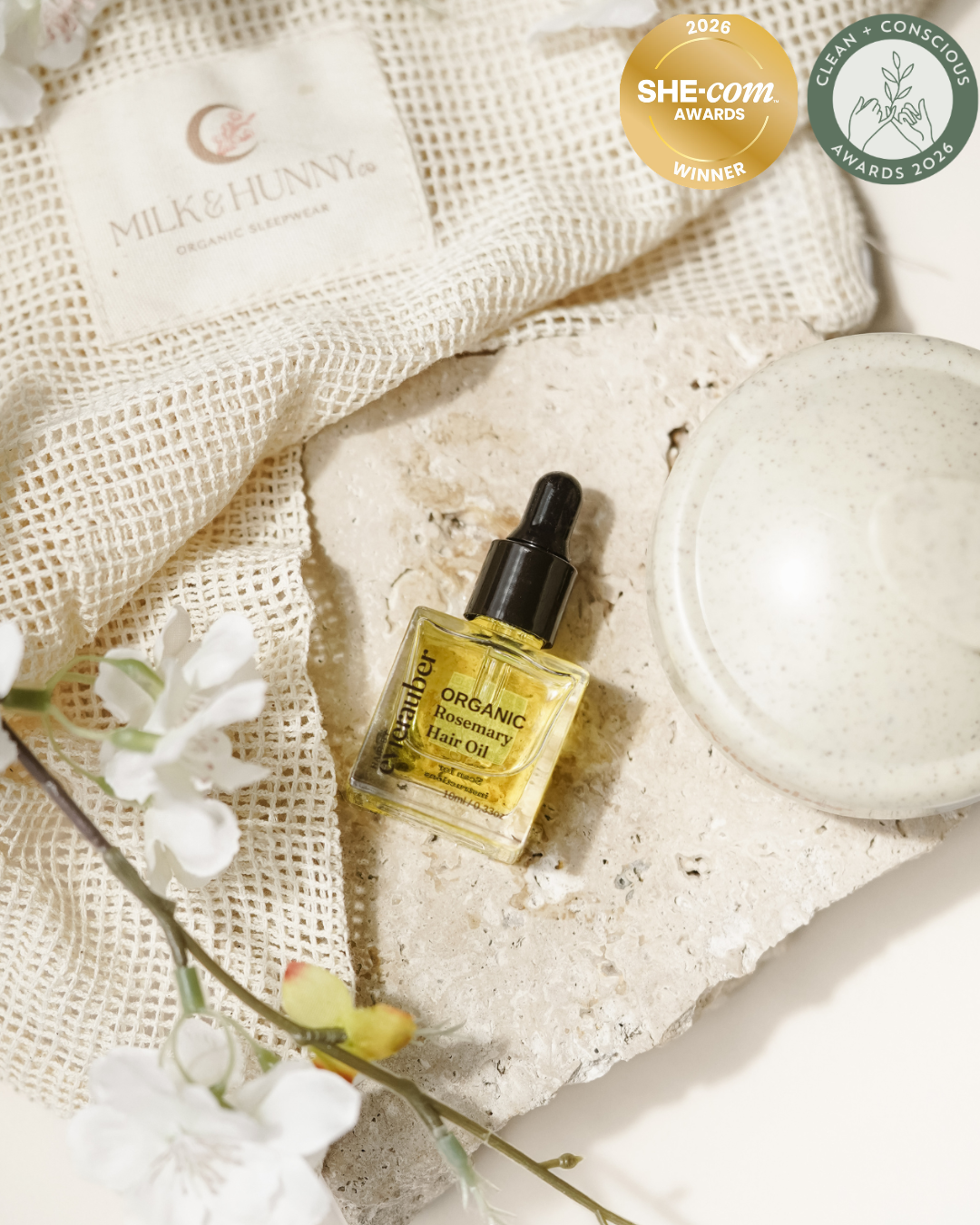 A bottle Rosemary Organic hair, styled on a textured stone slab with a brand patch, and white blossoms. 